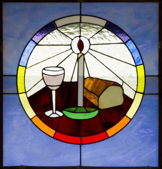 This picture is of a stained glass window, showing a lit candle, bread and wine. Around it, a circle showing rainbow colours.